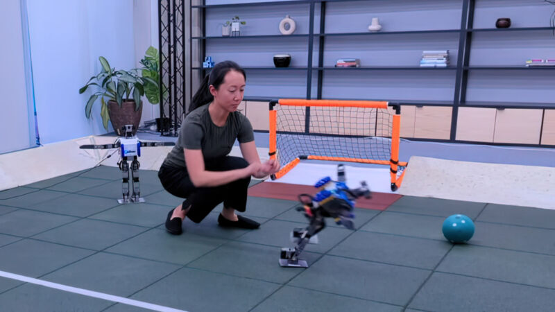 En una imagen fija de un video de demostración de DeepMind, un investigador empuja un pequeño robot humanoide al suelo.