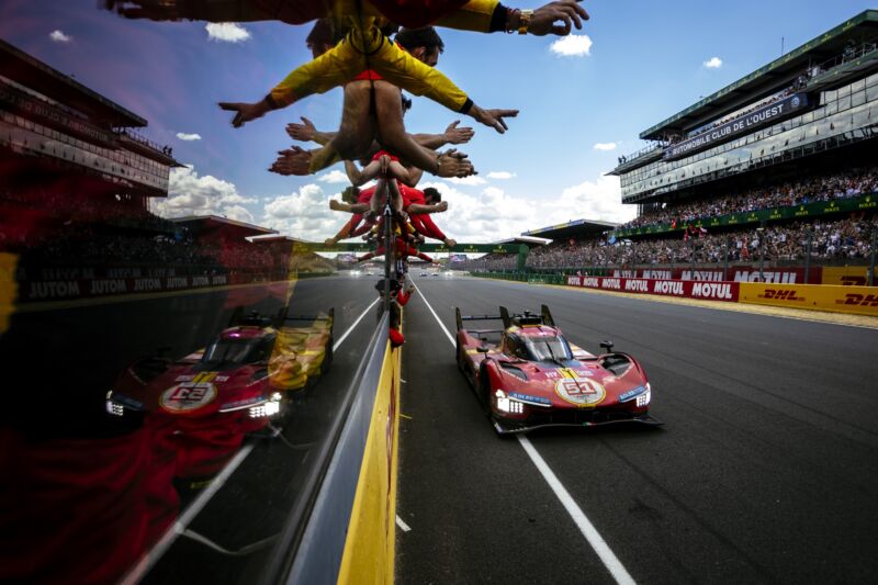A red Ferrari prototype drives past the pit wall at Le Mans as the team celebrates