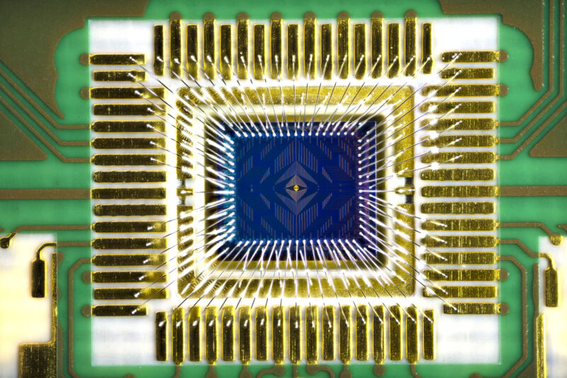 Image of a small black chip surrounded by golden wiring and a green circuit board.