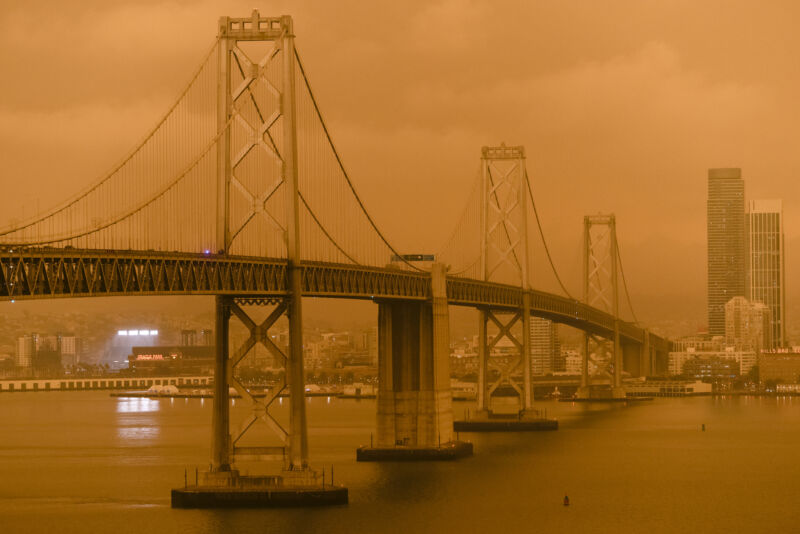 Image of an orange sky with a bridge and buildings partly obscured in the haze.