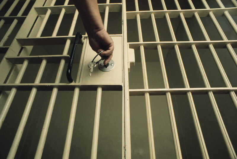 The bars of a jail cell are pictured along with a man's hand turning a key in the lock of the cell door.