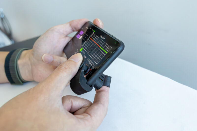 Image of a hand pressing its thumb into a black plastic cell phone attachment.