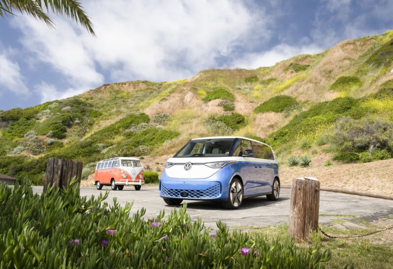 A blue VW ID Buzz and an orange VW T2 with some wildflowers in the foreground