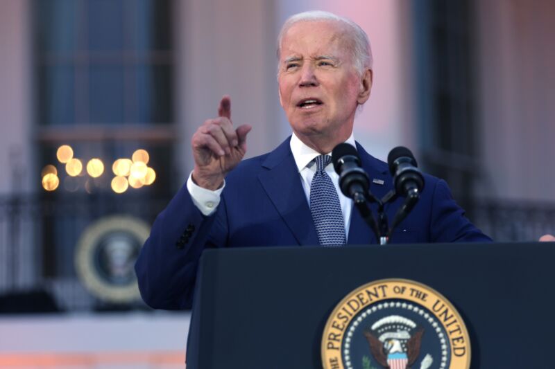 President Joe Biden points to his right hand and speaks into microphones at a podium set up outside the White House.