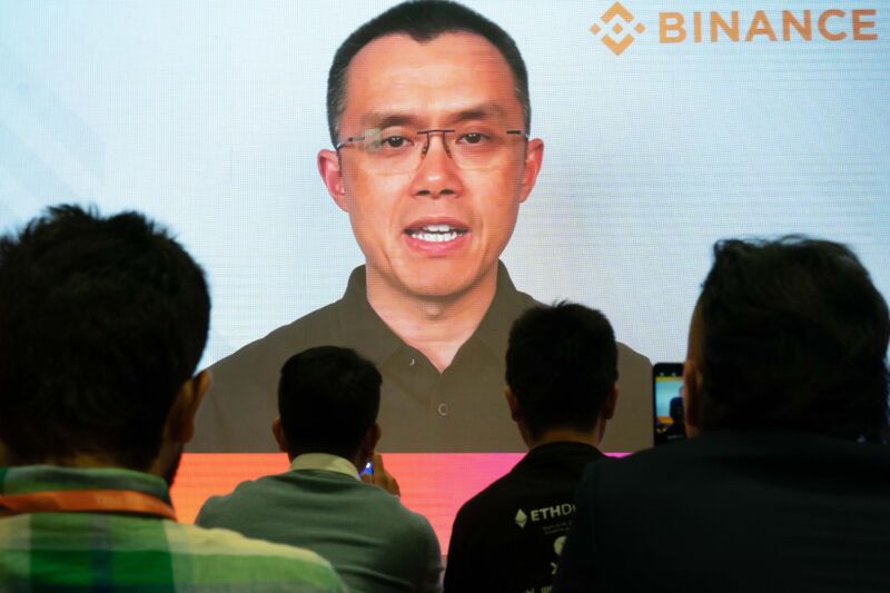 An audience at a conference watches Binance CEO Changpeng Zhao speaking on a large video screen.
