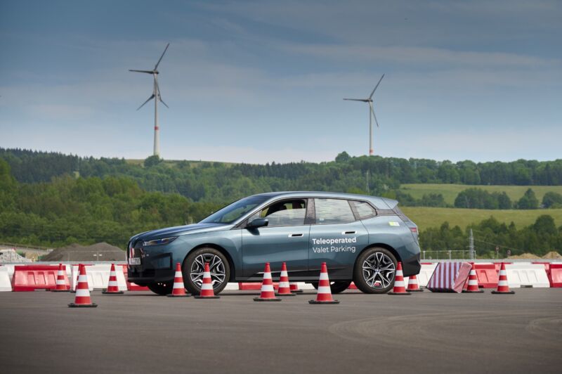 A blue BMW iX at a test track with wind turbines in the distance