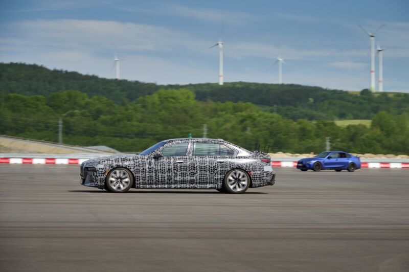 A camouflaged BMW i7 and a blue BMW M3 drive autonomously around a test track in the Czech Republic.