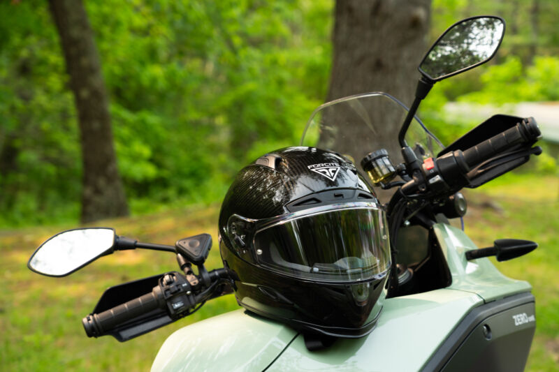 A black motorcycle helmet rests on the seat of an electric motorcycle in the woods