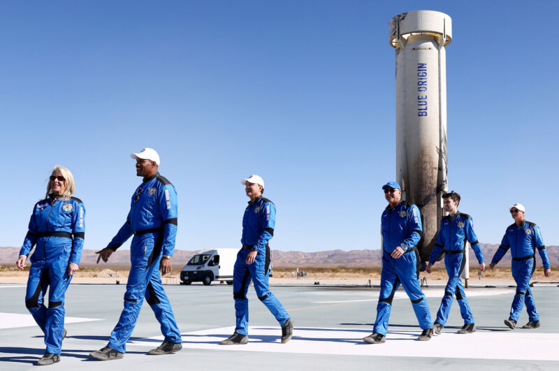 A crew of six passengers, including former professional football player and television anchor Michael Strahan, stroll past the Blue Origin New Shepard booster they rode into space in December 2021.