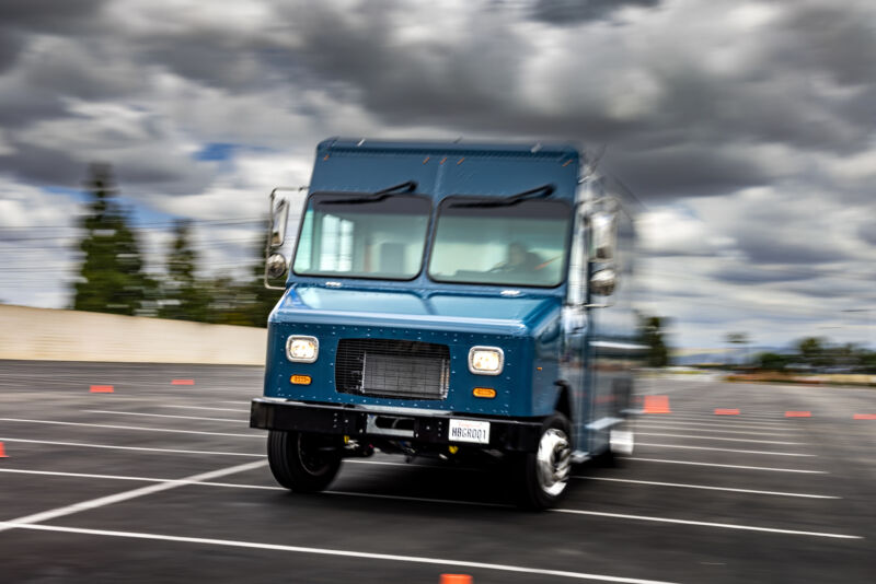 A blue package truck drives past the camera under leaden skies