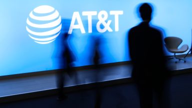 People at a conference walk by a large AT&T logo.