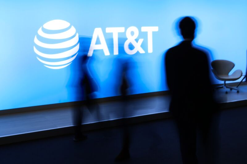 People at a conference walk by a large AT&T logo.
