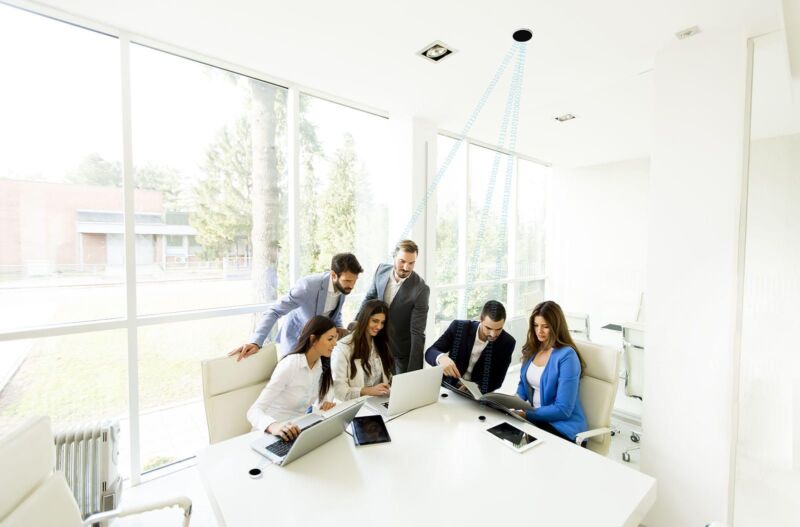 People gathered around a signal-emitting light point on the ceiling in an office