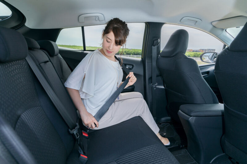 A woman sitting in the back seat of a car fastens her seatbelt