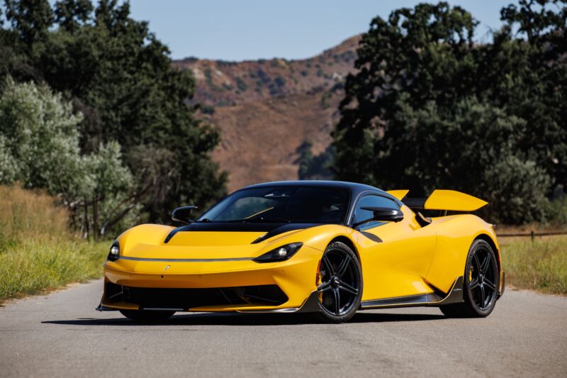 A yellow pininfarina Battista parked with mountains in the background