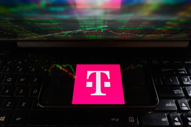 In this photo illustration a T-Mobile logo is displayed on a smartphone while a laptop screen displays a stock market chart.