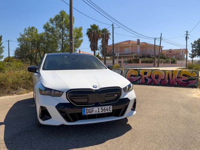 A white BMW i5 M50 parked next to a jersey barrier with colorful graffiti on it