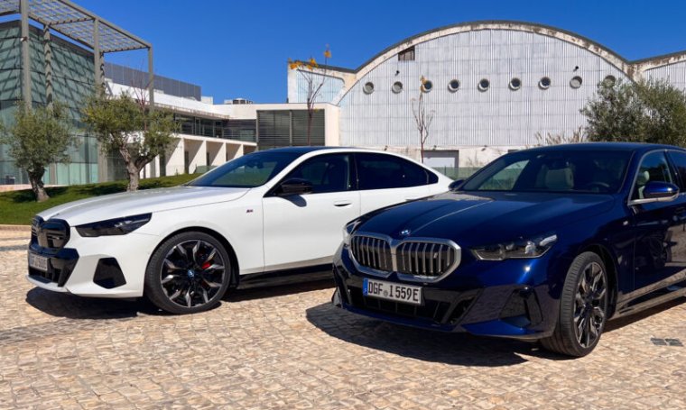 A pair of BMW i5s, one white, one metallic blue, parked outside a modern building