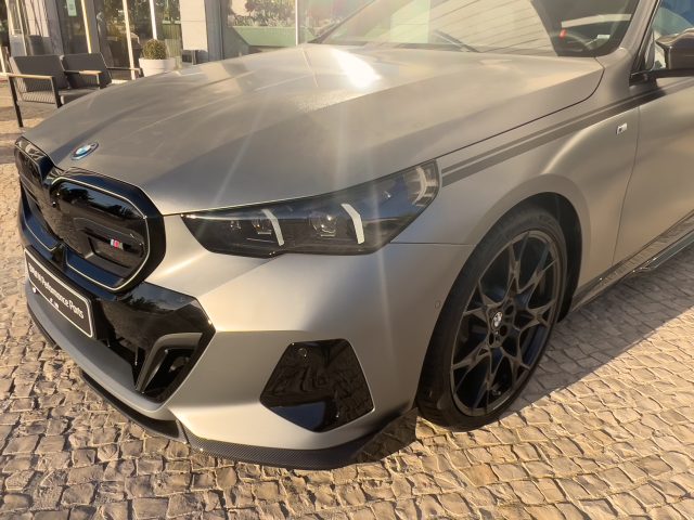 A matte silver BMW i5 adorned with carbon fiber accessories like a front splitter