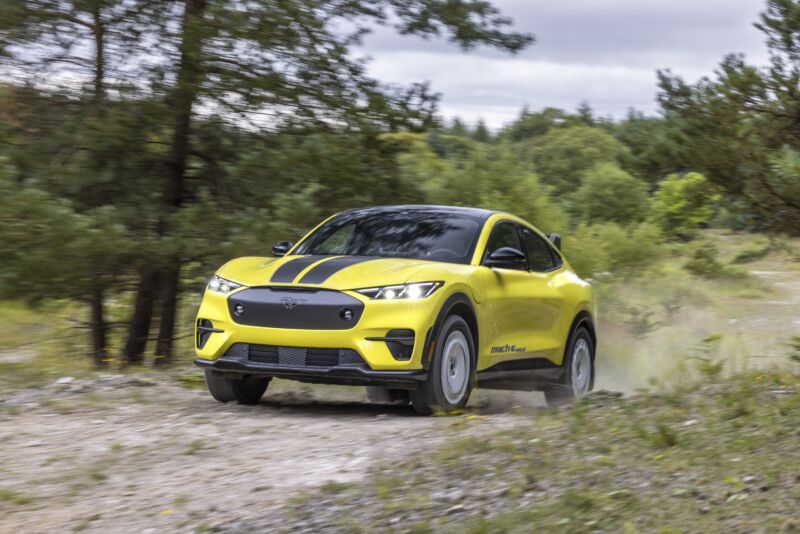 A yellow ford mustang mach-e rally driving on a dirt road