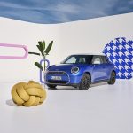 A blue mini Cooper with a giant knot next to it and patterns on some walls