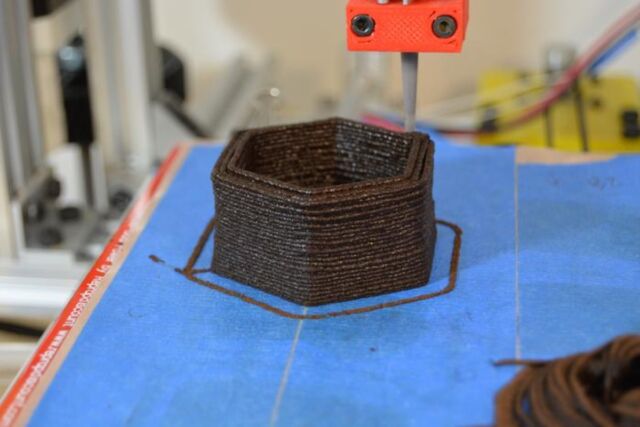 A modified 3D printer fabricates a flower planter from used coffee grounds.
