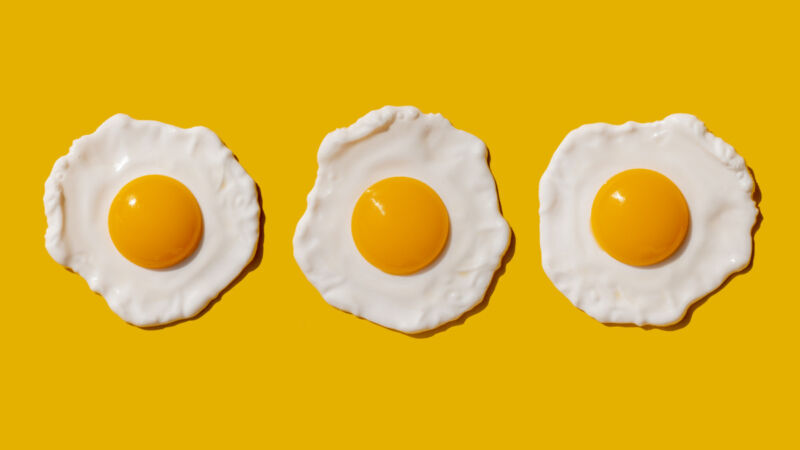 Three fried eggs in a row on a yellow background.