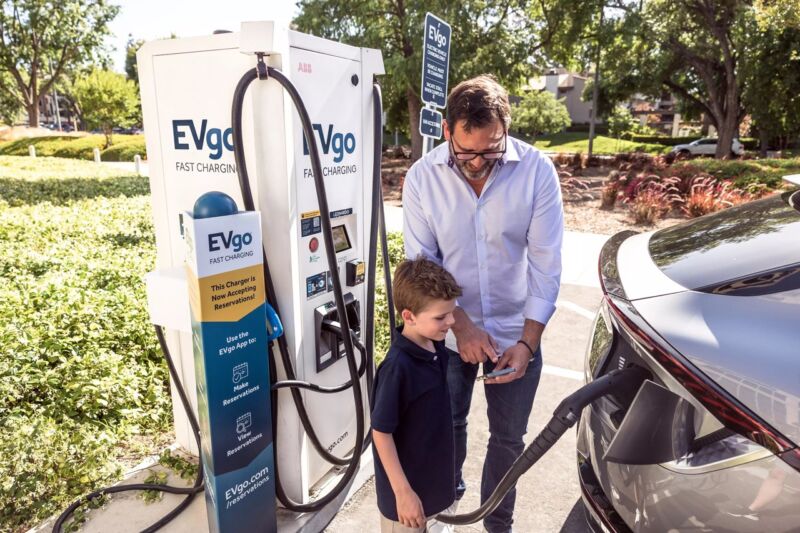 Man showing his son the EVgo app while charging a car