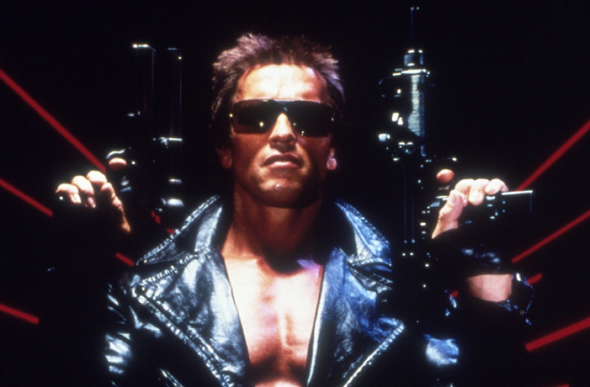very muscular man in a leather jacket, bare-chested and wearing sunglasses, with a gun in each hand
