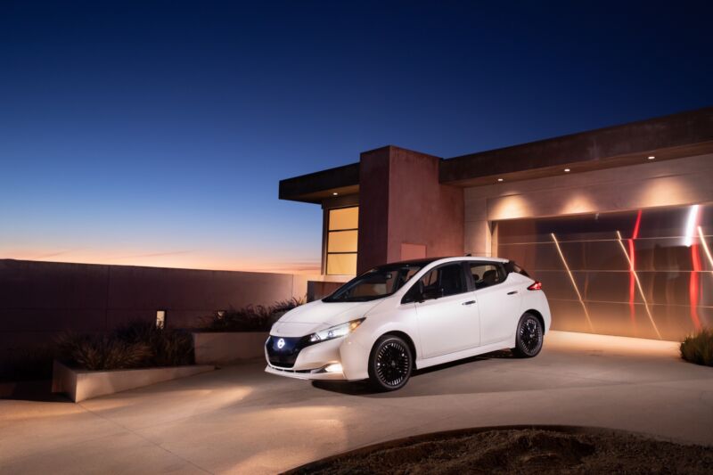 A white Nissan Leaf parked outside a modern house in the desert at night.