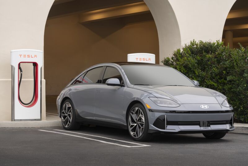 A grey Hyundai Ioniq 6 is parked next to a Tesla Supercharger