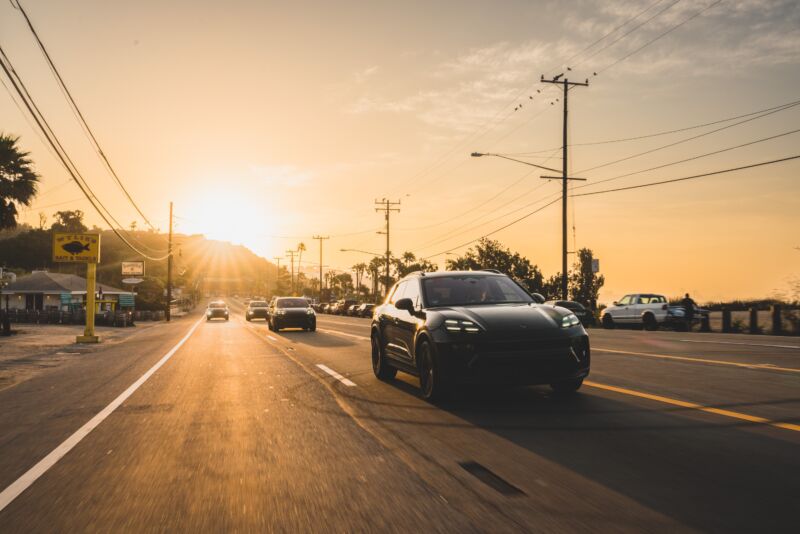 Several black Porsche Macan prototypes drive east away from the setting sun