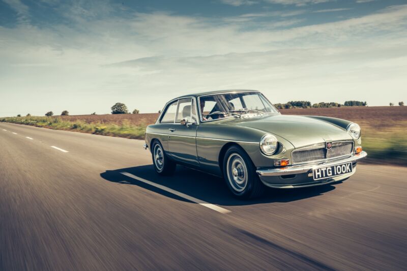 A metallic green MGB drives down an English road