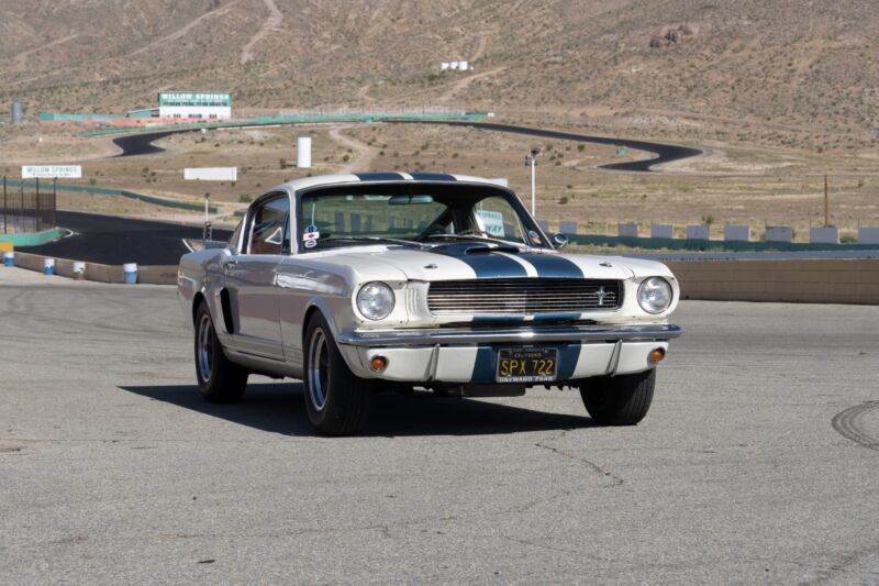 A white Ford Mustang GT350 restomod with blue stripes, with the mountains of Willow Springs in the background