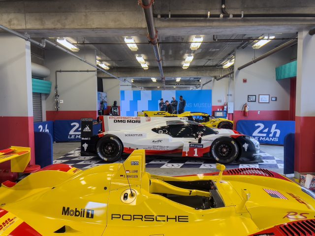 A garage with racing cars. In the foreground is the Porsche RS Spyder, with the 919 Hybrid and 963 in the background