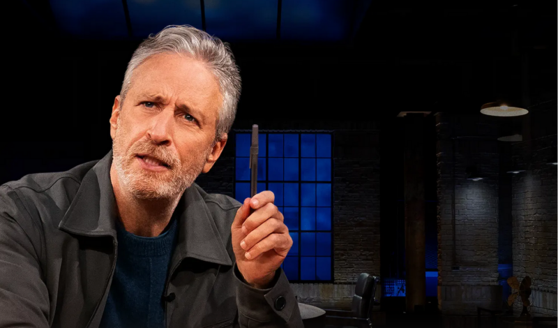 Jon Stewart holds up a pen as he makes a point at his dsek