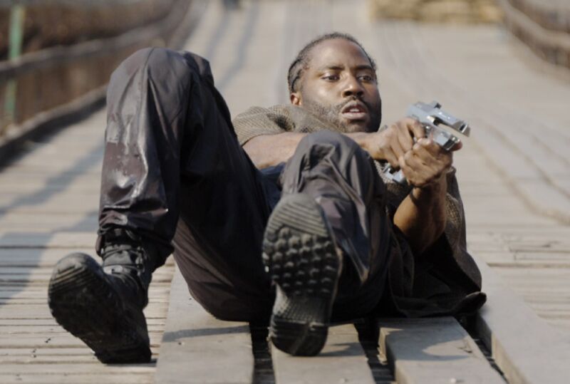 black man lying in road on back pointing a gun