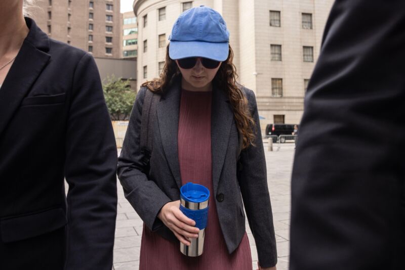 Caroline Ellison walks toward a courthouse wearing a baseball cap and carrying a thermos.