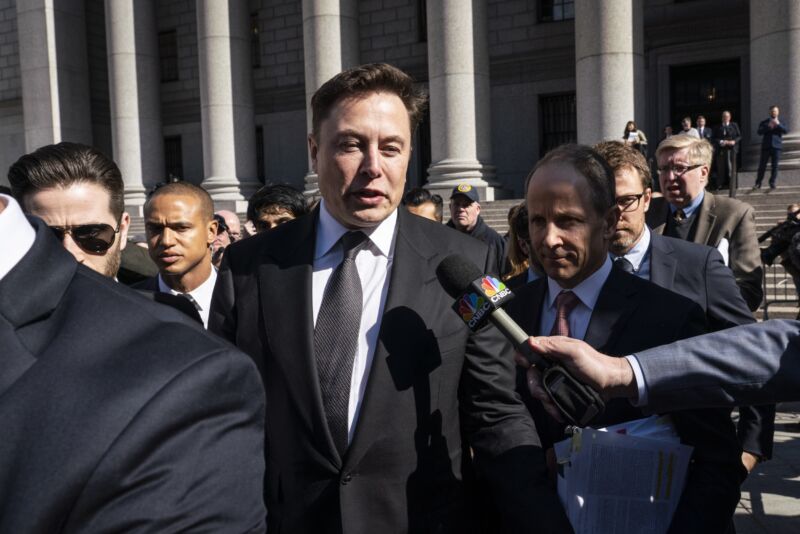 Elon Musk walks out of a federal courthouse and speaks to reporters as a member of the media holds a microphone.