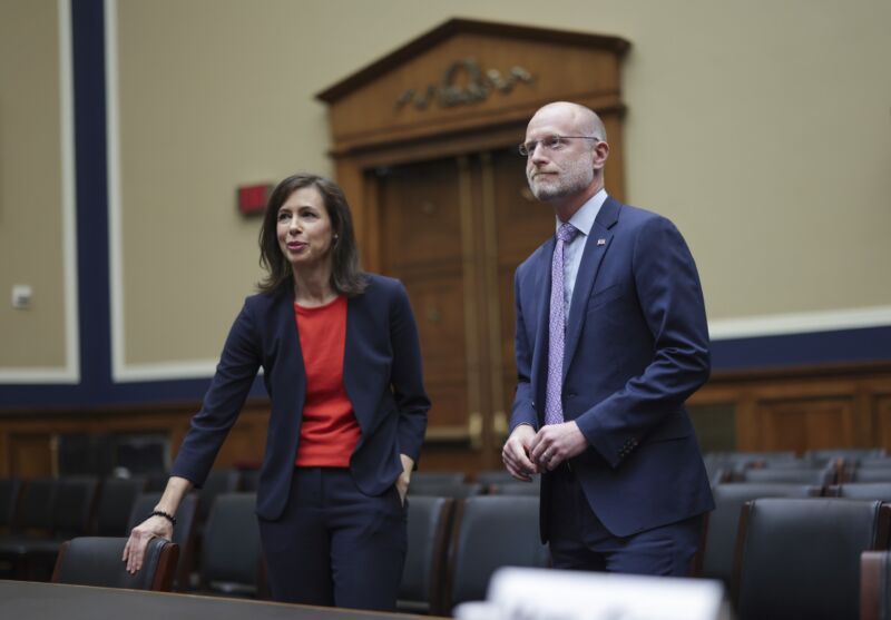 FCC Chairwoman Jessica Rosenworcel and FCC Commissioner Brendan Carr stand next to each other in a Congressional hearing room before a hearing.