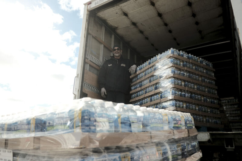 Muncitorii orașului descarcă un camion care conține paleți de apă îmbuteliată pentru a-i distribui în timpul unui eveniment de distribuție a filtrului de apă din 26 octombrie 2021 în Hamtramck, Michigan.  Departamentul de Stat pentru Sănătate și Servicii Umane a început să distribuie rezidenților filtre de apă și apă îmbuteliată din cauza nivelurilor ridicate de plumb găsite în apa potabilă din cauza conductelor de apă vechi și neîntreținute din oraș.