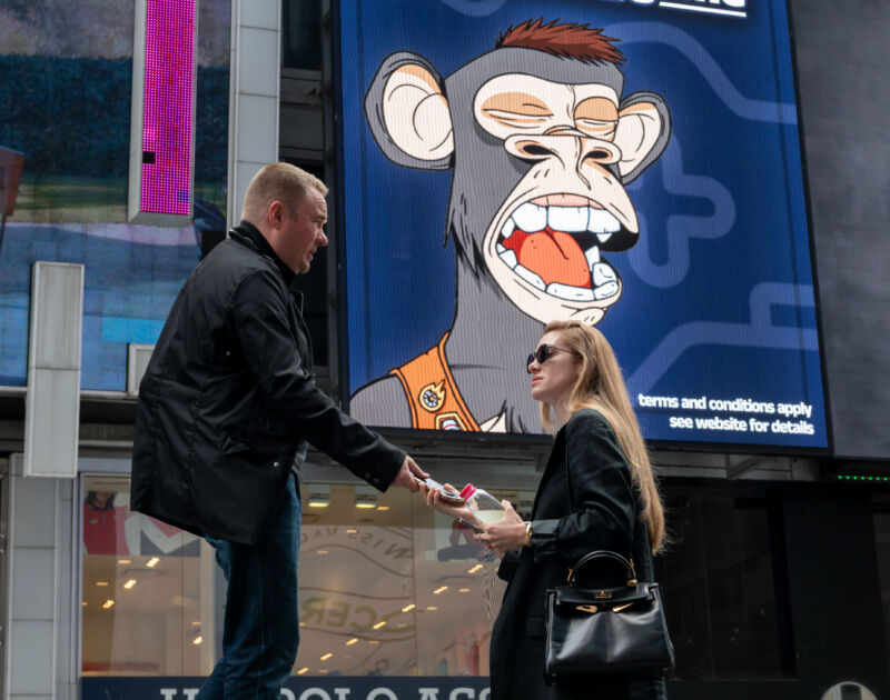 People walk by a Bored Ape Yacht Club NFT billboard in Times Square on June 23, 2022 in New York City. Sunglasses would have been a good idea for this year's ApeFest.