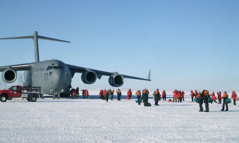 Image of a large aircraft parked on the snow, with people milling nearby.