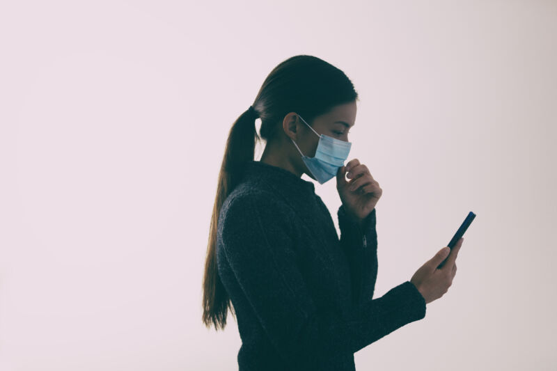 A woman wearing a face mask and checking her phone.