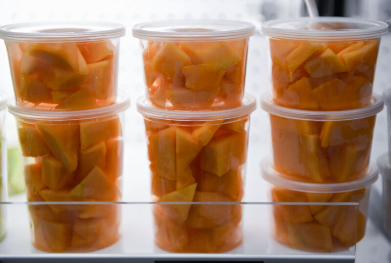 Containers with cut cantaloupe in a cooler case.