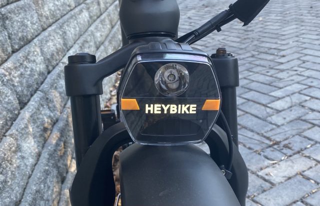 Image of a headlight perched on top of a wheel, with orange lights on either side of it.