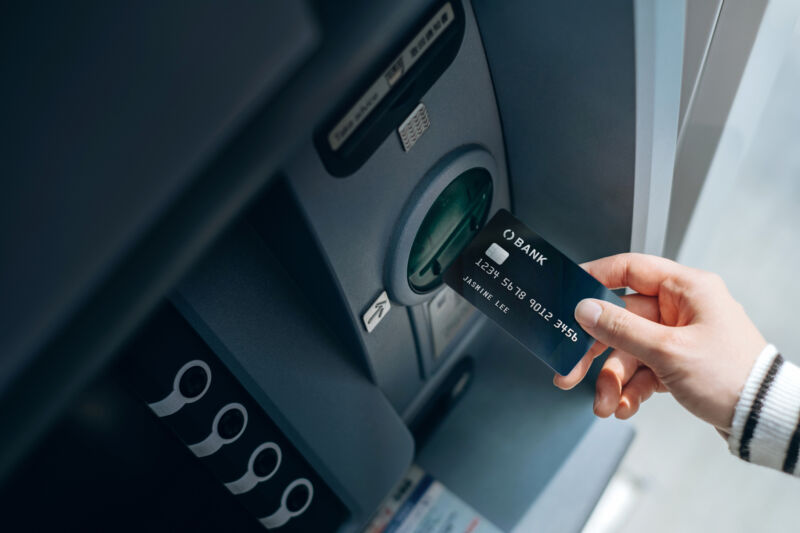 High angle shot of female hand inserting her bank card into automatic cash machine in the city. Withdrawing money, paying bills, checking account balances and make a bank transfer. Privacy protection, internet and mobile banking security concept