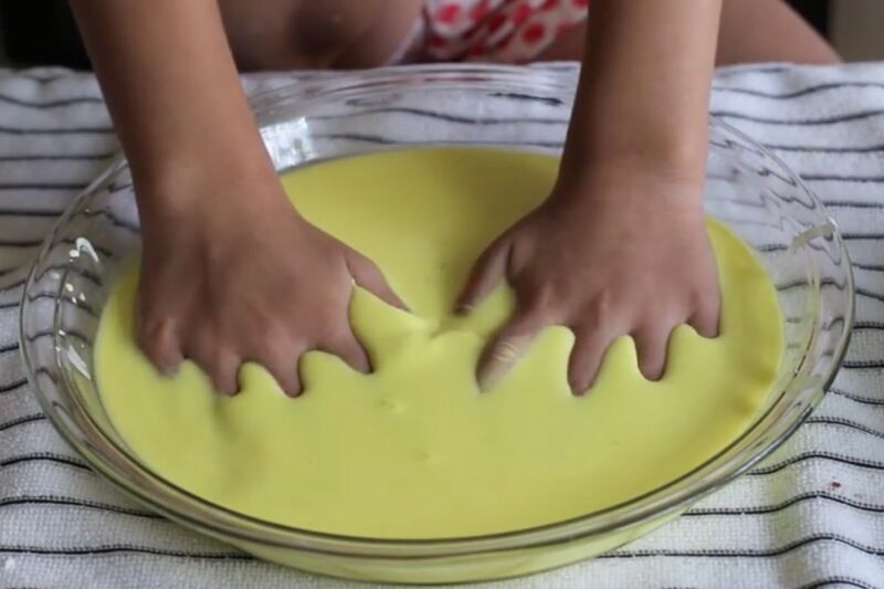 Mâinile copilului stoarce o substanță lipicioasă galbenă într-un bol de sticlă.