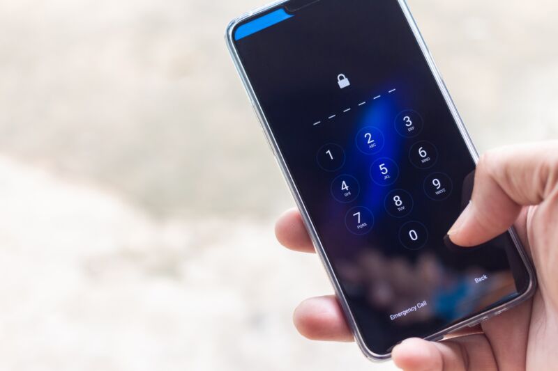 A person's hand holding a smartphone while entering the screen-lock passcode.