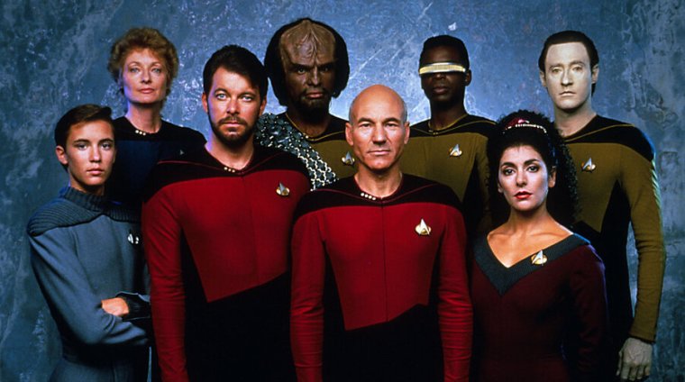 Actors in starfleet uniforms pose in a line with Patrick Stewart in the middle
